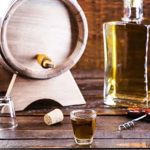 Photo d'un petit tonneau en bois, une bouteille de cachaça ambrée et un verre rempli sur une table en bois, illustrant différentes options de cachaça artisanale.