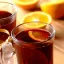 Deux tasses de Glühwein avec des rondelles d'orange sur une table en bois, accompagnées d'une poignée dorée.