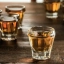 Trois verres à shot remplis d'une boisson ambrée, posés sur une table en bois sombre.