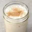 Verre en mason rempli de rum milk punch crémeux, garni d'une pincée de muscade râpée sur le dessus.