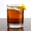 Un verre de cocktail Rusty Nail avec glaçons et une spirale de zeste de citron sur le bord.