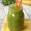 Smoothie vert au kiwi, servi dans un pot Mason avec deux pailles orange, entouré de kiwi frais et de banane.