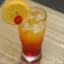 Un verre à cocktail rempli d'un mélange de teintes rouges et oranges, garni d'une tranche d'orange et d'une cerise.