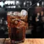 Un grand verre rempli de Jack Daniel's et de Coca-Cola, garni de glaçons et servi avec une paille noire.