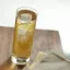 Verre haut rempli d'un cocktail ambré, surmonté de glaçons, posé sur une table en bois.