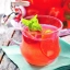 Verre de punch cranberry pétillant avec rondelles d'orange et feuille de menthe sur serviette verte, distributeur en arrière-plan.