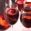 Quatre verres de sangria remplis de vin rouge et de tranches d'orange flottantes.