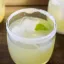 Verre de cocktail rempli d'un mélange jaune clair avec des glaçons, garni d'une tranche de citron vert et un bord givré de sucre.