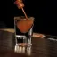 Un verre à shot rempli d'un cocktail brunâtre, un liquide est versé doucement à partir d'une bouteille.