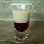 Un verre à shooter rempli d'une liqueur crèmeux beige et d'une couche de liqueur rouge foncé, avec un bord du verre givré.