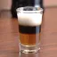 Un verre à shot avec un cocktail en trois couches distinctes, composé de crème, liqueur foncée et une base de couleur ambrée.