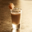 Verre à shot transparent rempli de cocktail crémeux beige, garni d'un cube de caramel sur une pique.