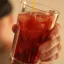 Gros plan sur une main tenant un verre rempli de glaçons et d'un cocktail rouge profond, en train d'être mélangé.