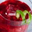 Gros plan d'un verre de cocktail Kool Aid Slammer rouge vif, garni d'un cube de glace et d'un zeste de citron vert en spirale.