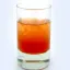 Un verre contenant un cocktail coloré rouge et orange sur fond blanc.