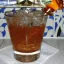 Un verre de cocktail Royal Flush rempli de glaçons, avec une garniture de zeste d'orange en spirale sur un cure-dent, posé sur une serviette blanche, sur un fond avec des motifs bleus et blancs.