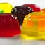 Plusieurs jello shots colorés et brillants disposés sur une surface blanche.